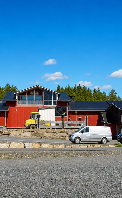 A red timber commercial building and gravel yard beside pine forest in the village of Lappi, Satakunta.