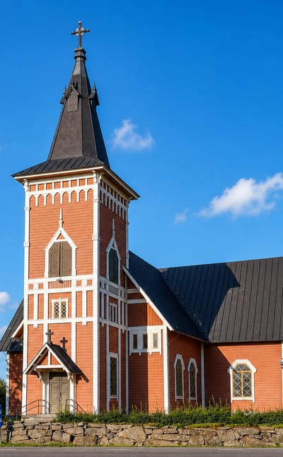 Vampula's red wooden church with a tall black steeple rising above a stone churchyard wall under a blue summer sky, Finland.