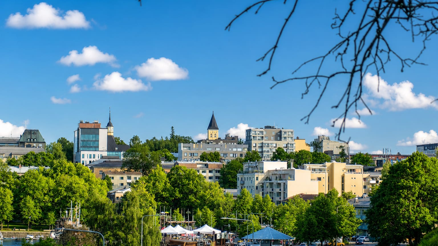 Lappeenranta summer skyline with a clock tower above green treetops and a lakeside harbour with white market tents