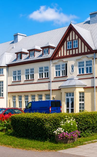 Cream and red half-timbered spa-era building in Kylpylä, Lappeenranta, with flower beds and clipped hedges.