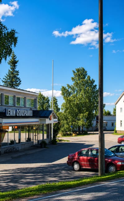 Village street with the Lemi cooperative bank building, parked cars and summer birches in Lemi, Finland.