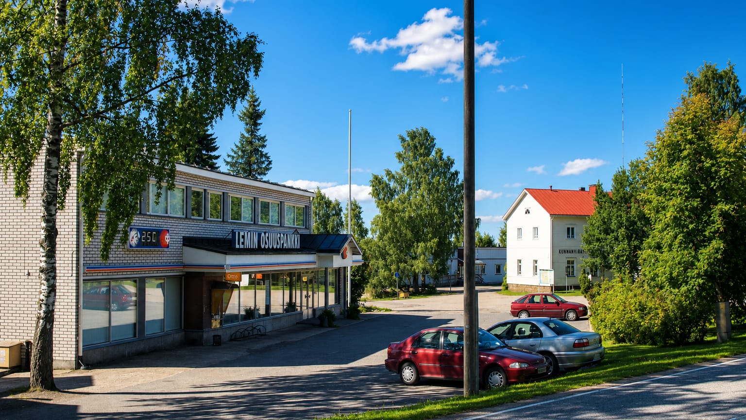 Village street with the Lemi cooperative bank building, parked cars and summer birches in Lemi, Finland.