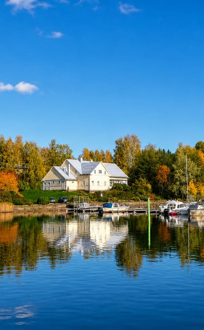 Lakeside marina at Taipalsaari, Finland, with small boats moored on calm Lake Saimaa beneath autumn birch trees.