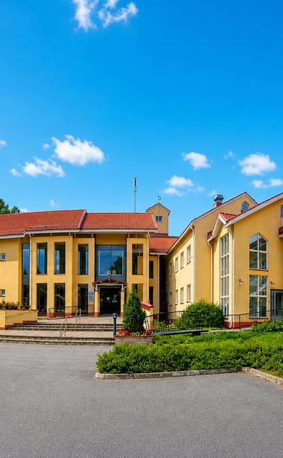 A yellow municipal building with a red-tiled roof and forecourt in Ahtari, Finland, under a blue sky.