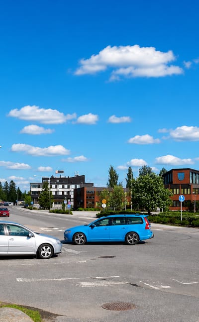 Town-centre intersection with parked cars and a red-brick civic building in Alavus, Finland.