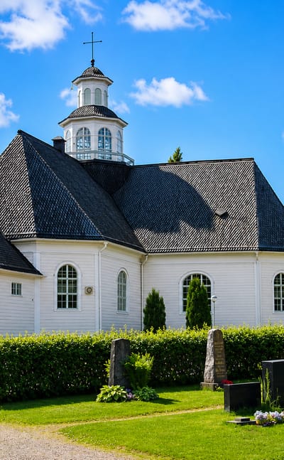 White wooden church with shingle roof and lantern tower beside its graveyard in Ilmajoki, Finland.