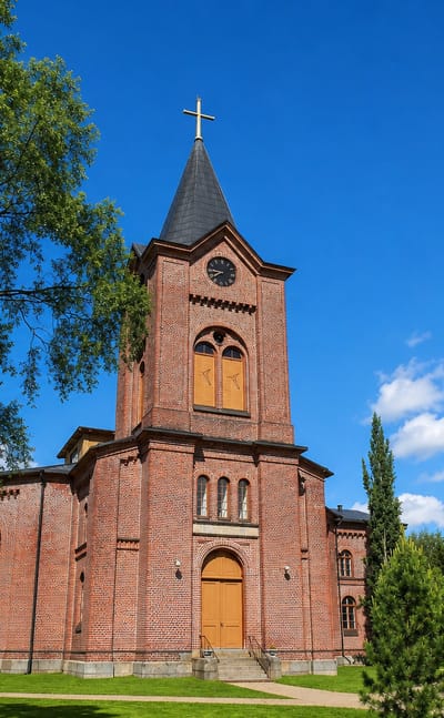Red-brick church with a slender spire and clock tower under a blue sky in Isokyrö, Finland.