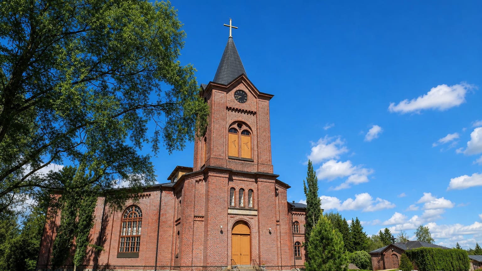 Red-brick church with a slender spire and clock tower under a blue sky in Isokyrö, Finland.
