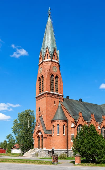 Red-brick neo-Gothic church with a tall green spire under blue sky in Kauhava, Finland