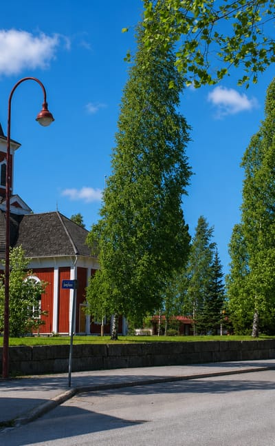 Red wooden church and separate bell tower framed by birch trees along a street in Kortesjärvi, Finland.