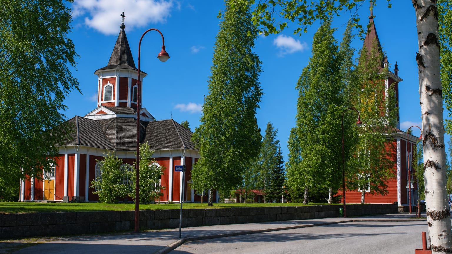 Red wooden church and separate bell tower framed by birch trees along a street in Kortesjärvi, Finland.