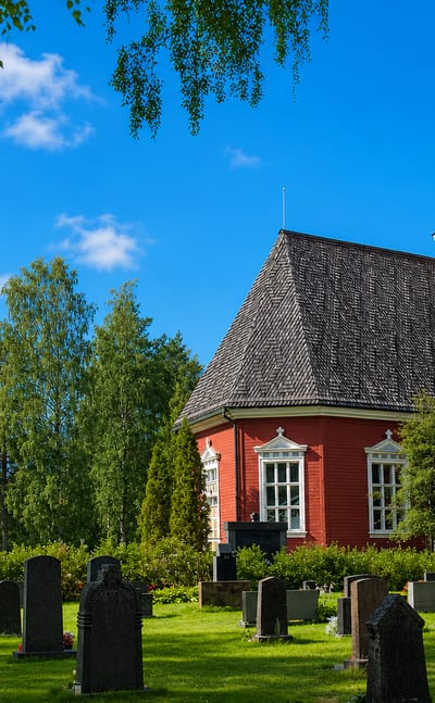 Red wooden Kuortane church and separate yellow bell tower rising above the graveyard in Kuortane, Finland.