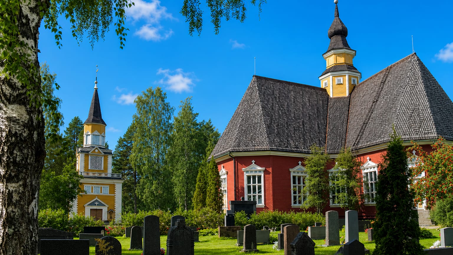 Red wooden Kuortane church and separate yellow bell tower rising above the graveyard in Kuortane, Finland.