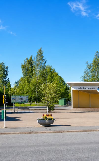 Teuva town-square pavilion lettered Taito teuvalainen and Aito teuvalainen with a kiosk and birch trees