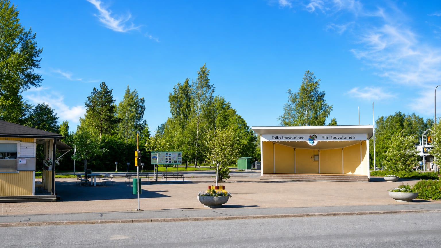 Teuva town-square pavilion lettered Taito teuvalainen and Aito teuvalainen with a kiosk and birch trees