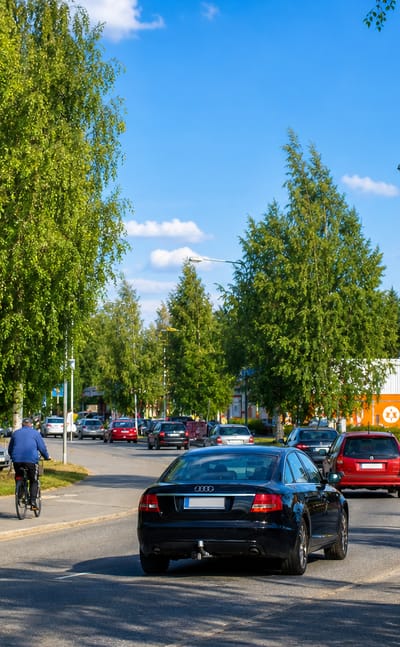 Tree-lined main street with cyclists, parked cars and a supermarket in Vimpeli, Finland.