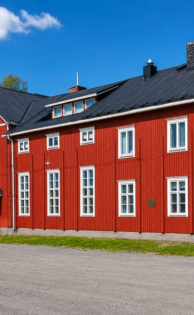 A large traditional red-and-white Ostrobothnian timber building beside a gravel yard and forest in Ylihärmä, Finland.