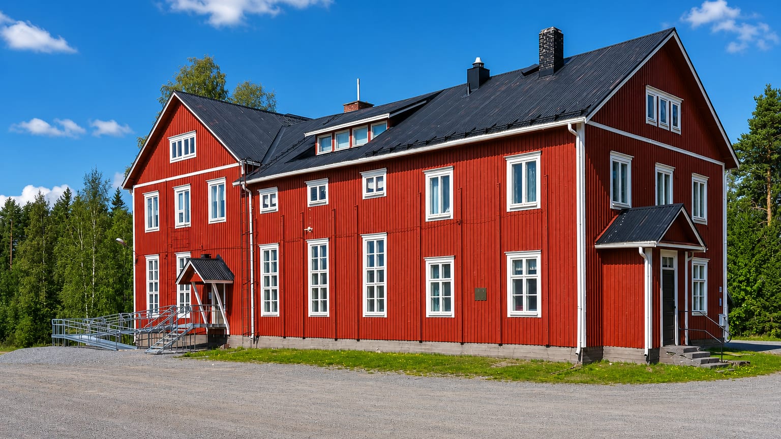 A large traditional red-and-white Ostrobothnian timber building beside a gravel yard and forest in Ylihärmä, Finland.