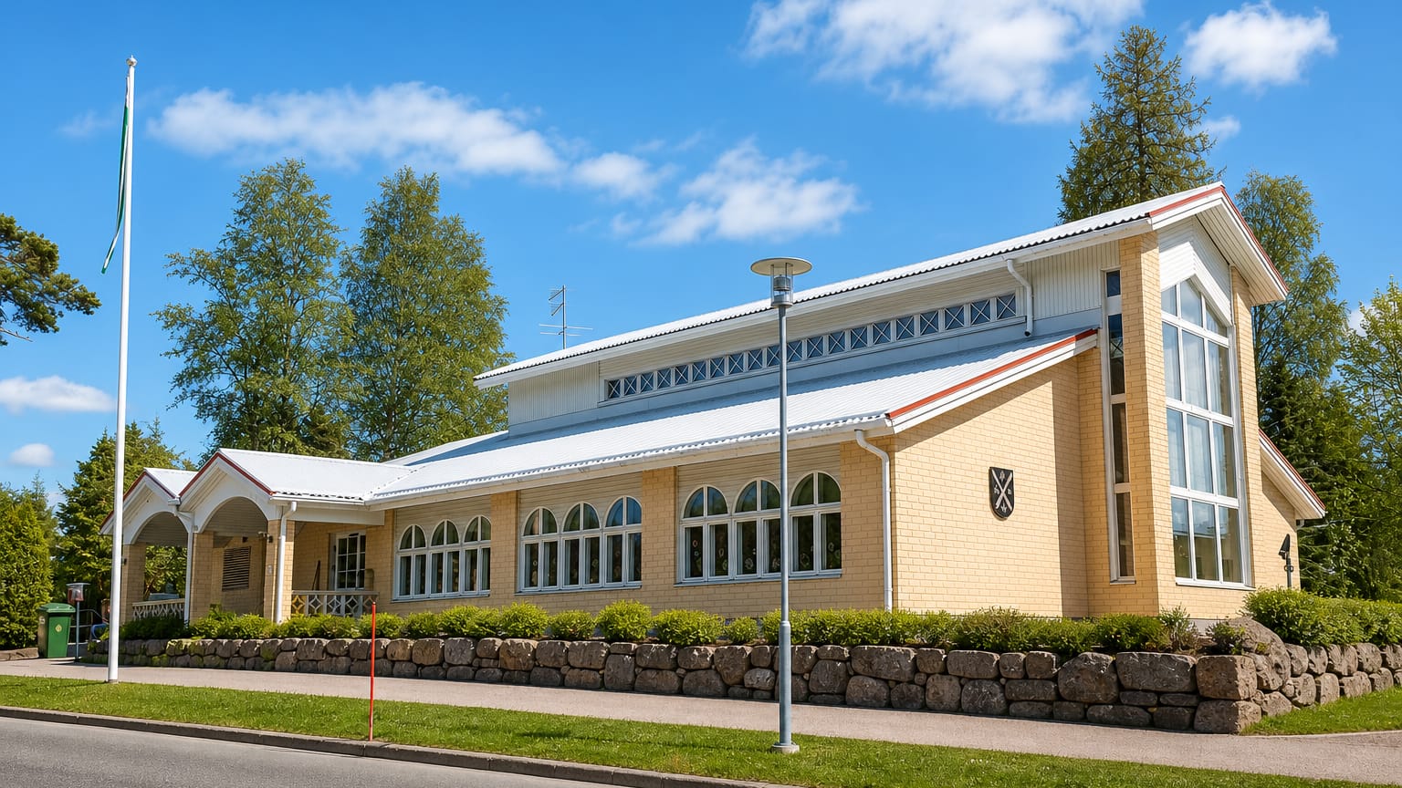 Modern yellow-brick community hall with arched windows and a crested facade in Enonkoski, Finland.