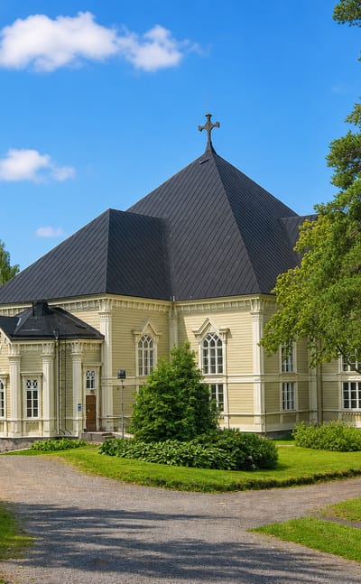 Kangasniemi's yellow wooden church with a dark octagonal roof and cross, framed by birches and a gravel path.