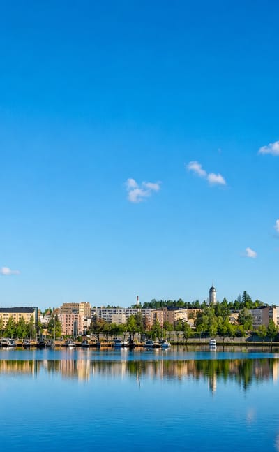Mikkeli's lakeside townscape across Savilahti bay, with low buildings and a church spire under a blue summer sky.