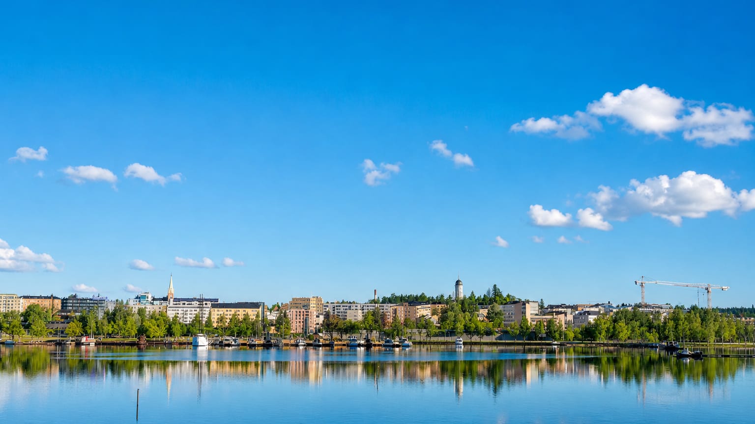 Mikkeli's lakeside townscape across Savilahti bay, with low buildings and a church spire under a blue summer sky.