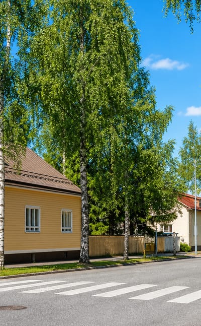 Yellow wooden house and birch-lined street with a crossing in Nuijamies, Mikkeli, in summer.