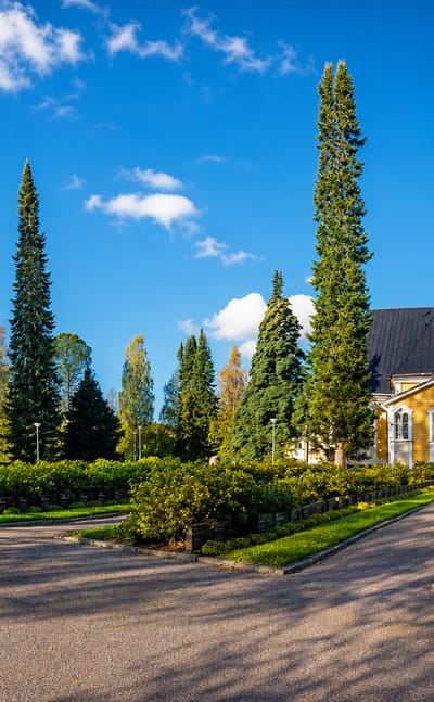 Pieksämäki's yellow wooden church and detached red bell tower among autumn trees under a clear blue sky, Finland
