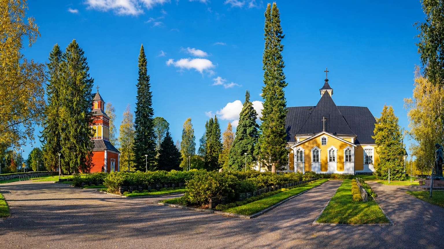 Pieksämäki's yellow wooden church and detached red bell tower among autumn trees under a clear blue sky, Finland