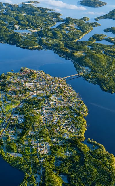 Aerial view of Puumala village on a forested peninsula amid Lake Saimaa's islands in Finland, a bridge crossing the strait.