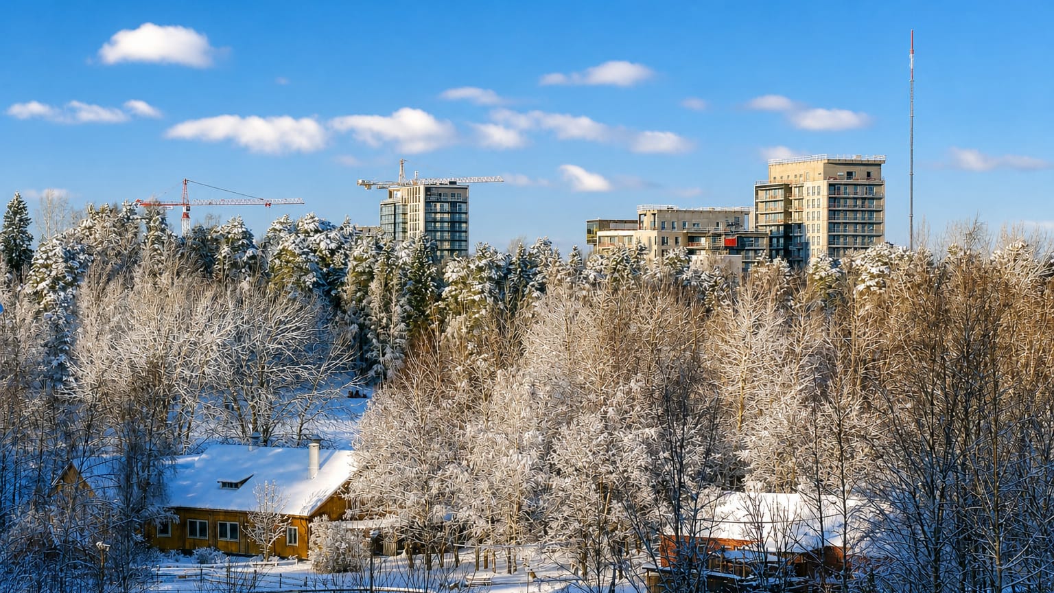 Snow-covered forest and a wooden house below modern apartment towers and construction cranes in Espoonlahti, Espoo, Finland