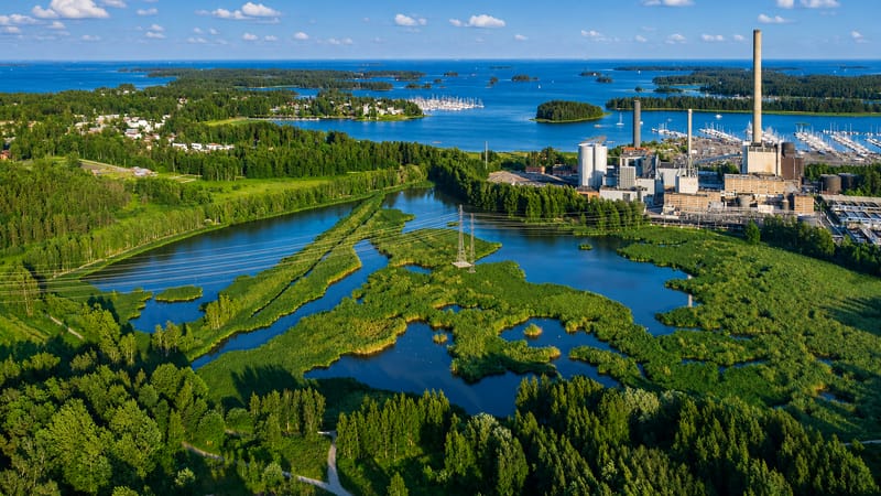 Aerial view of Espoo's green coastal wetlands, a marina and power-plant chimney beside the Gulf of Finland archipelago