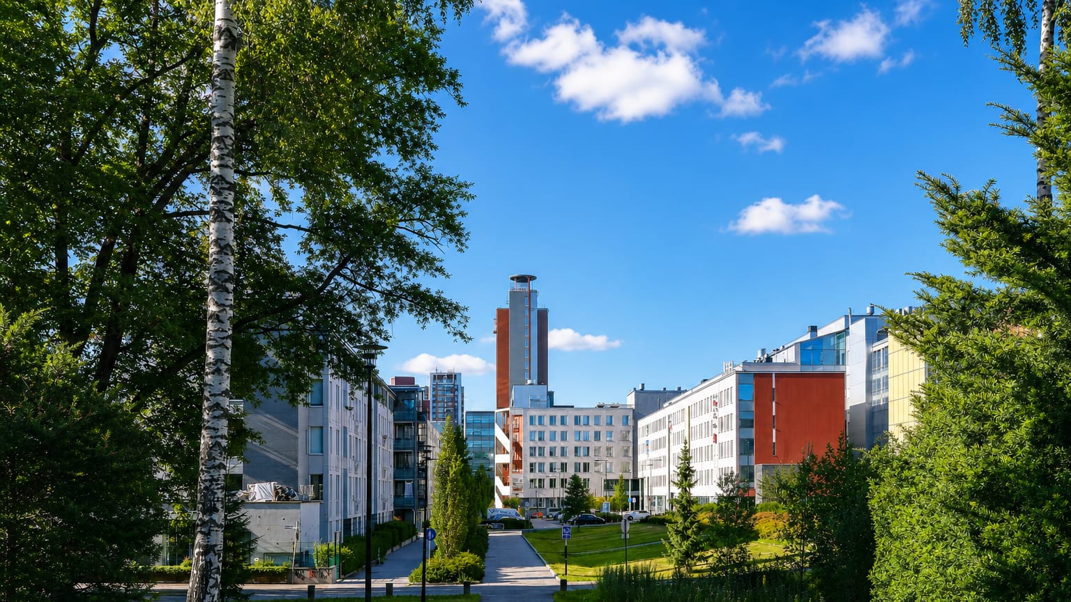 Modern apartment and office blocks and a slim tower beyond a birch-lined park path in Leppävaara, Espoo, Finland