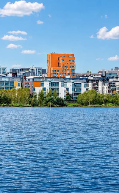 Arabianranta's colorful modern waterfront apartment blocks lining the green shore of Vanhankaupunginlahti bay in Helsinki under a blue sky