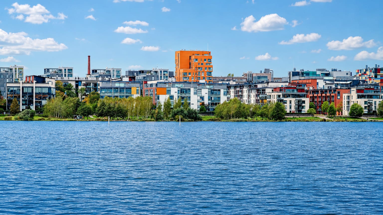 Arabianranta's colorful modern waterfront apartment blocks lining the green shore of Vanhankaupunginlahti bay in Helsinki under a blue sky