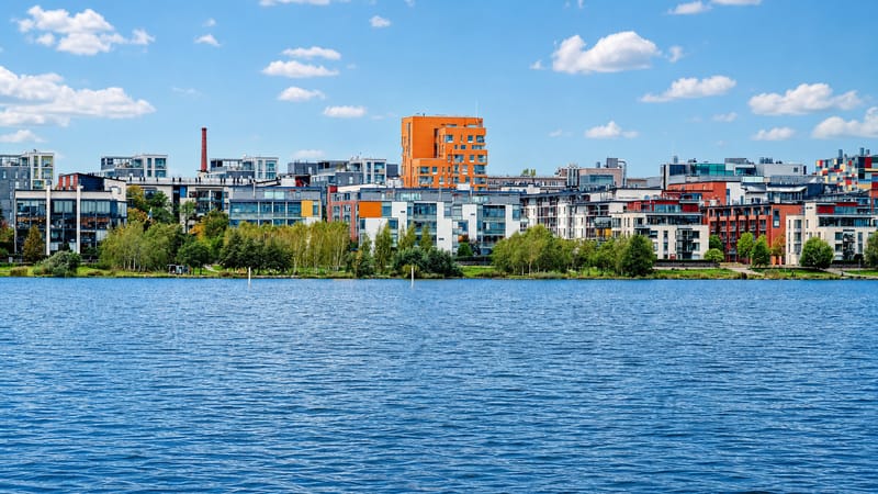 Arabianranta's colorful modern waterfront apartment blocks lining the green shore of Vanhankaupunginlahti bay in Helsinki under a blue sky