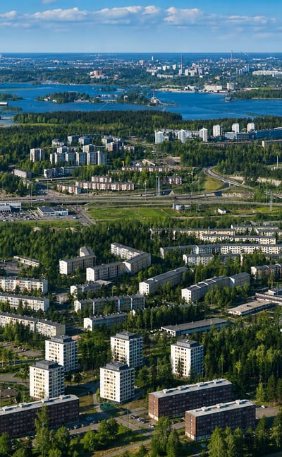 Aerial view of East Helsinki's suburban apartment districts amid forest and sea inlets, with the central Helsinki skyline on the horizon