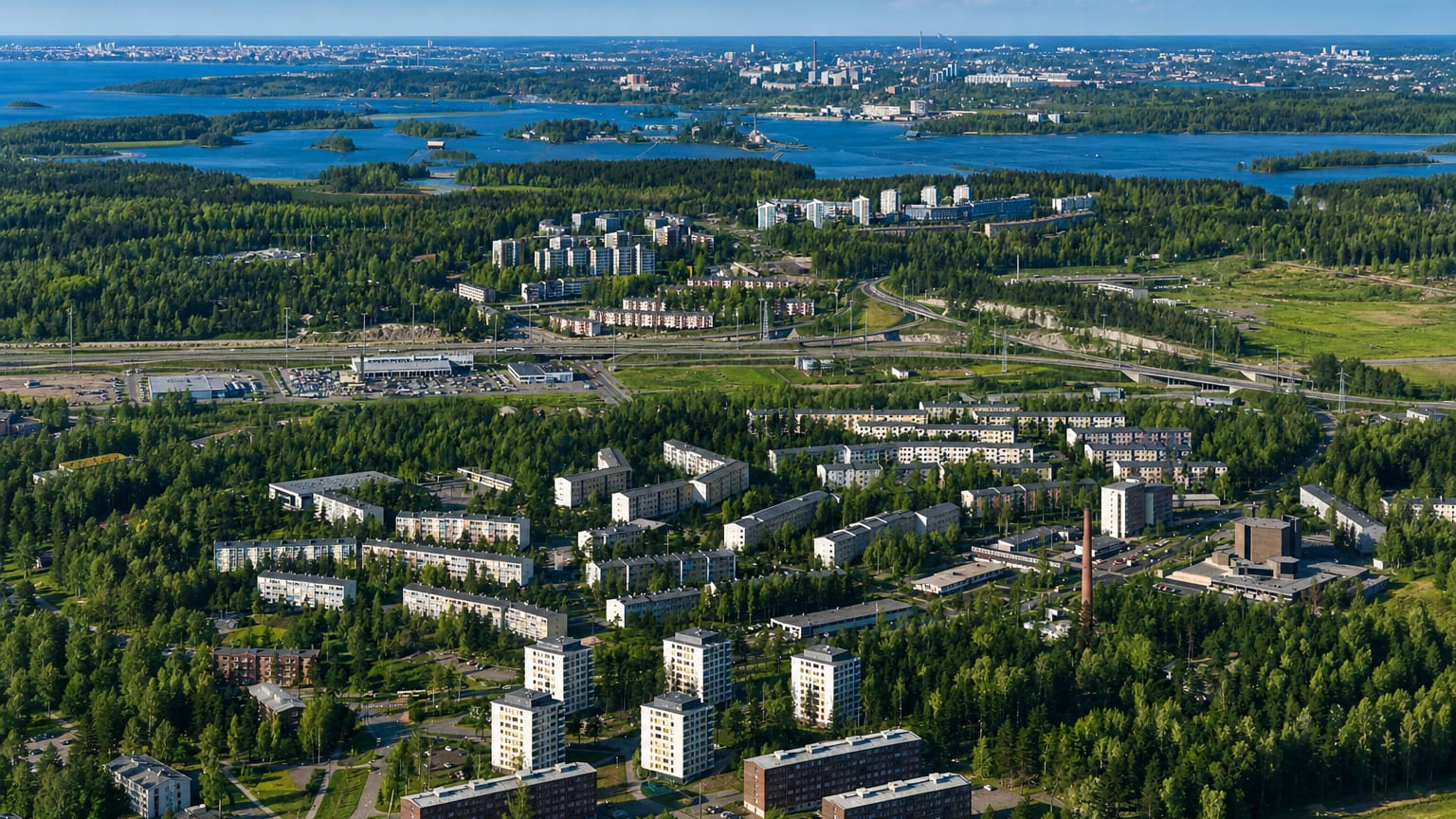 Aerial view of East Helsinki's suburban apartment districts amid forest and sea inlets, with the central Helsinki skyline on the horizon