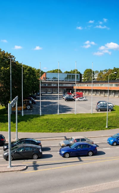 Road junction in Etelä-Haaga, Helsinki, with parked cars, flagpoles and a low brick commercial building