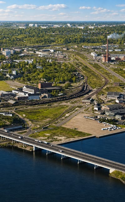 Aerial view of Hermanni, Helsinki, a coastal district with a road bridge over a bay, low-rise blocks and a tall chimney