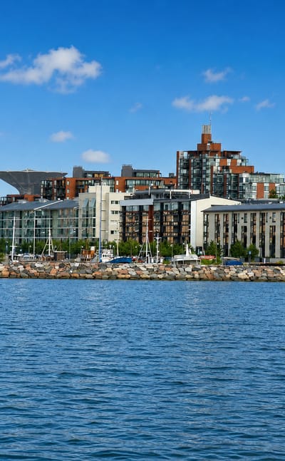Modern waterfront apartment blocks along the rocky shoreline of Herttoniemenranta, Helsinki, seen across a calm sea bay.