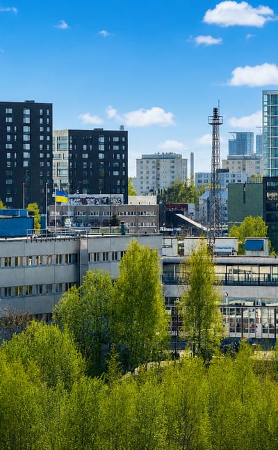 Herttoniemi's modern apartment towers and low industrial blocks rising above birch-covered green slopes in eastern Helsinki