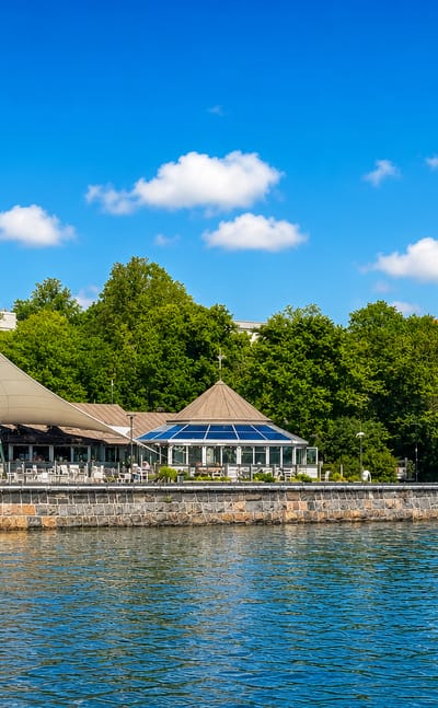 Waterfront cafe pavilion and stone seawall along the shore of Kaivopuisto park in Helsinki on a sunny summer day.