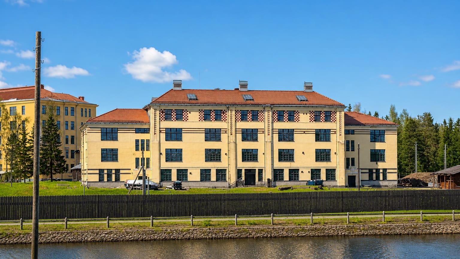 A large yellow three-story building with a red-tiled roof beside a canal under blue sky in Käpylä, Helsinki, Finland.