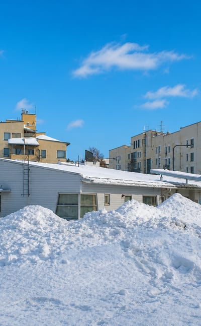 Snow-covered low-rise yellow apartment blocks and birch trees under a clear blue sky in Kivikko, Helsinki, in winter
