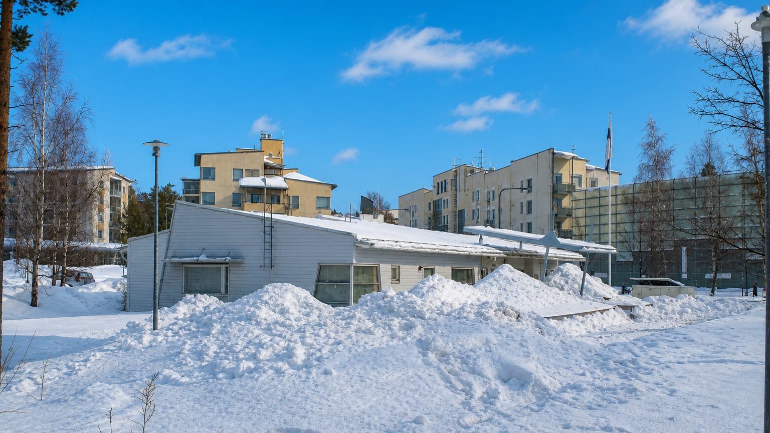 Snow-covered low-rise yellow apartment blocks and birch trees under a clear blue sky in Kivikko, Helsinki, in winter