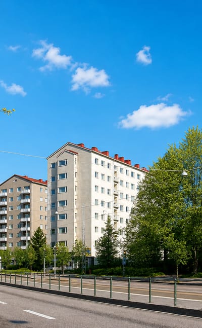 Sunlit apartment blocks along a tree-lined boulevard in Laakso, Helsinki, under a clear blue sky.