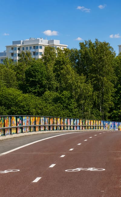 Mural-lined cycle bridge leading past birch woods and white apartment blocks in Länsi-Herttoniemi, Helsinki.