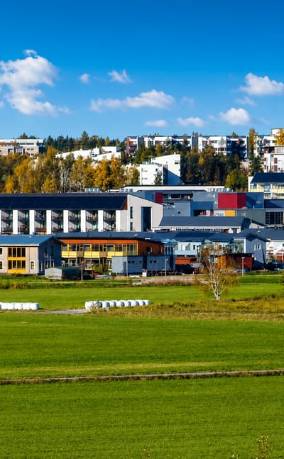 Modern apartment blocks of Latokartano, Helsinki, rising above autumn trees and a green field under a blue sky.
