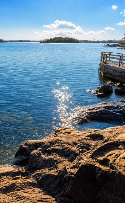 Rocky granite shoreline on Lauttasaari island in Helsinki, Finland, with a wooden pier and forested Baltic archipelago islets.